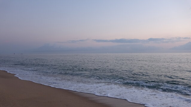 Cool Blue Dawn Seascape with Frothy Waves on Sandy Beach.
Large, active waves with abundant white foam and froth roll over the sandy beach shoreline in the foreground under pink sky in Gangneung.