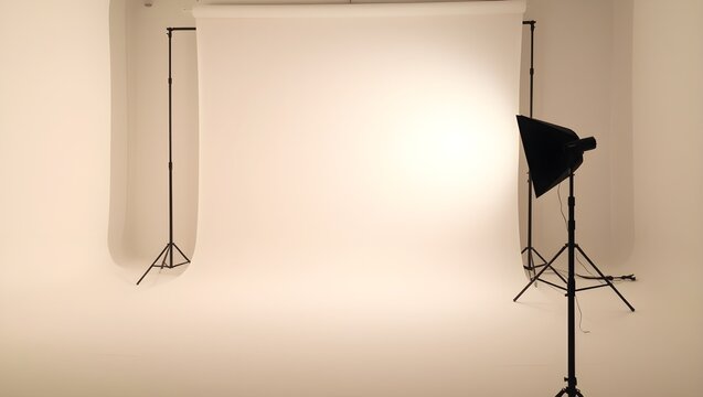 Empty professional photography studio with white backdrop and studio lighting equipment.