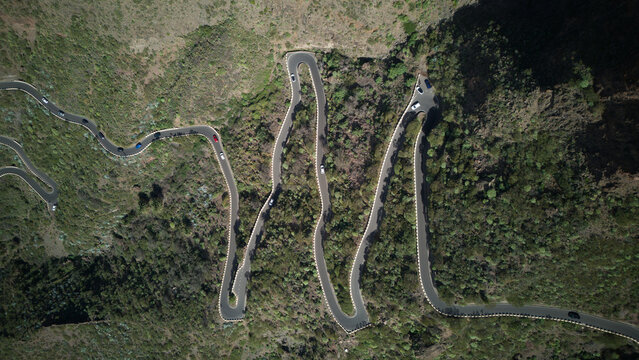 Aerial view of a winding mountain road with sharp switchbacks and cars driving through the rugged green landscape of Tenerife, Santa Cruz de Tenerife, Canary Islands, Spain.