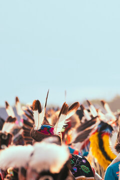 Colorful Native American powwow regalia and feathered headdresses at an outdoor cultural celebration, with bright blue sky and ample copy space.