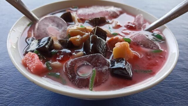 refreshing serving of classic Indonesian es campur, featuring shaved ice, colorful sweet ingredients, syrup, and condensed milk served in a traditional glass or bowl. This popular dessert showcases In