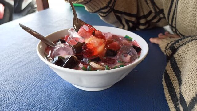 refreshing serving of classic Indonesian es campur, featuring shaved ice, colorful sweet ingredients, syrup, and condensed milk served in a traditional glass or bowl. This popular dessert showcases In