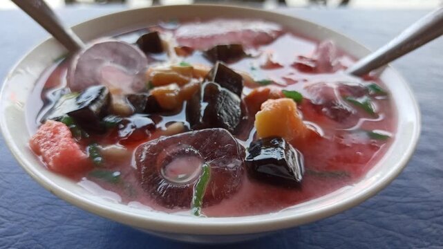refreshing serving of classic Indonesian es campur, featuring shaved ice, colorful sweet ingredients, syrup, and condensed milk served in a traditional glass or bowl. This popular dessert showcases In