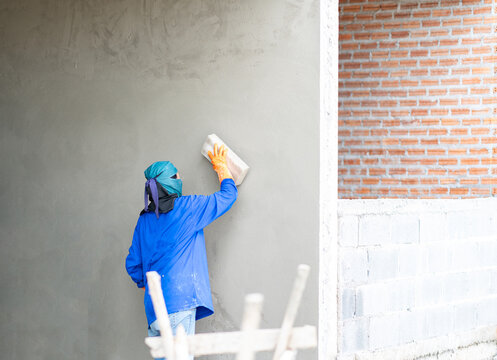 Back view of a plasterer finishing a grey concrete wall surface on a residential building site.