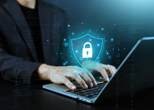 Businessman working on laptop with digital cyber security shield and padlock icon interface. Data protection, network safety, and information privacy concept on dark background with binary code.