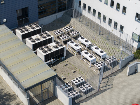 Aerial view of an AI data center cooling system with multiple industrial HVAC units arranged on a gravel rooftop next to a modern office building in Poland.