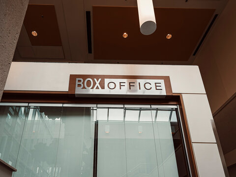 Modern architectural interior view featuring a sleek box office sign mounted on a textured wall with glass windows and warm ceiling lights