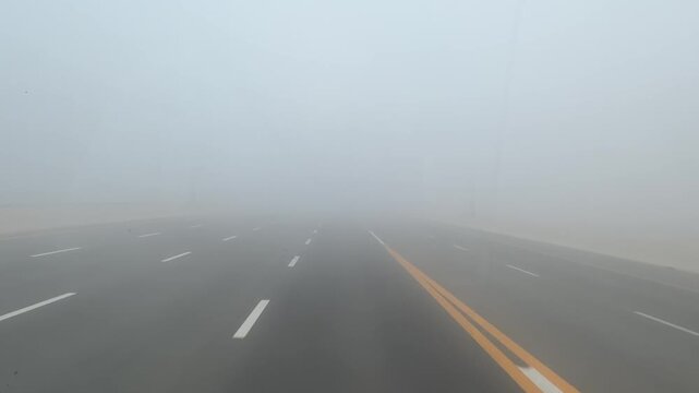 Vehicles move cautiously along a multi‑lane Abu Dhabi highway under extremely dense, low‑visibility fog.