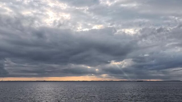 Panoramic overcast seascape with subtle sunbeams breaking through dense cloud layer for peaceful video backdrop