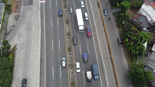 Top-down aerial drone view of vehicles and cargo trucks driving on a multi-lane highway toll road