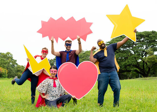Diverse group in superhero costumes holding colorful shapes outdoors.