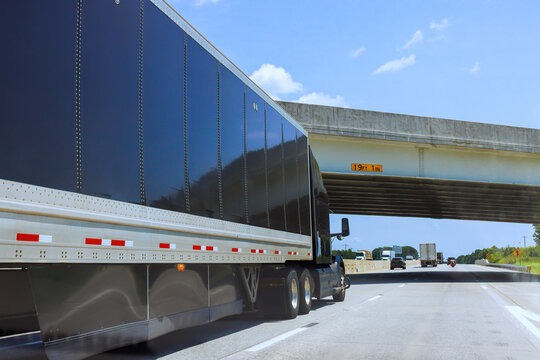 Large truck traveling on highway under bridge with height limit sign