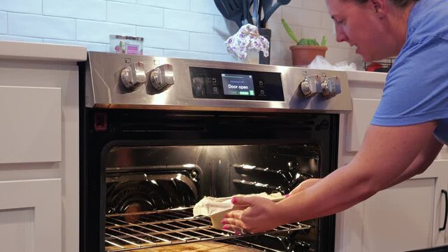 Woman scoring raw dough, taking a baked sourdough sandwich loaf out of oven, and rubbing butter over hot crust during homemade bread baking process