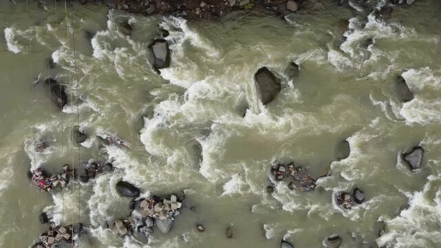 Top-down aerial view of turbulent muddy water rushing past river stones creating natural white water rapids