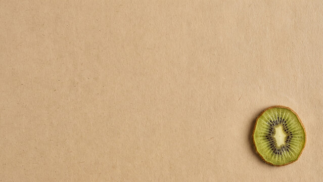 Dried kiwi slice placed in the bottom right corner of a plain brown kraft paper background