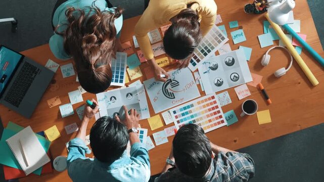 Top view of business team write graphic logo on meeting table with colorful sticky notes and design while explain idea. Project manager sharing idea and explain concept art to smart team. Symposium.