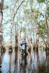 Person with camera stands near water in forest during daytime with trees surrounding them © 2B