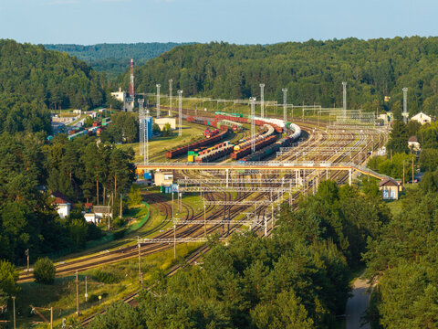 Aerial view of a large railway yard with freight trains and tracks surrounded by dense forest in Vilnius, Vilnius County, Lithuania.