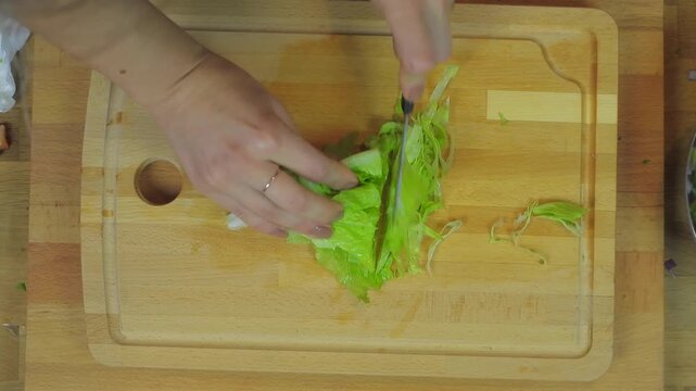 Woman chopping romaine lettuce on wooden cutting board during fresh kitchen meal prep.