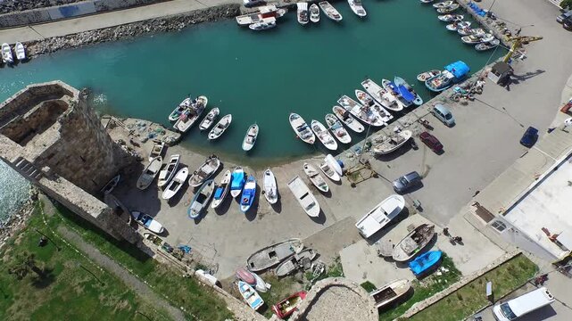Aerial view of historical castle walls and fishing boats at Mediterranean harbor.