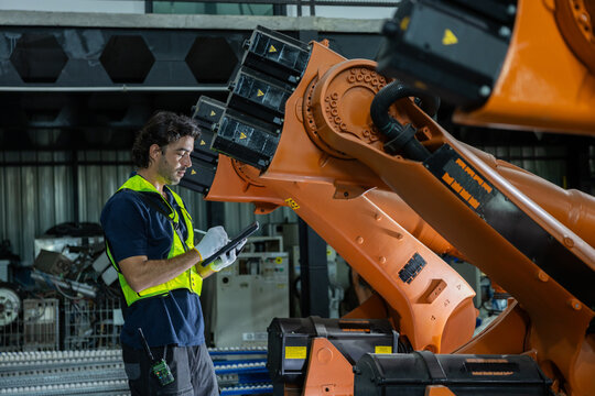 Industrial robot engineer factory tablet worker automation robotic arm safety vest inspection machinery industrial robot factory worker using tablet near orange robotic arm for automation