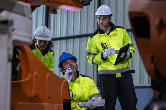 Industrial worker hard hat safety vest factory machinery engineer team inspection of equipment inside manufacturing plant with focused expression