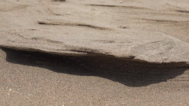 Wind shaped sand dune surface with carved ledge, natural erosion texture close view.