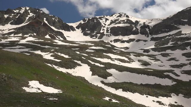 Spring alpine meadow with melting snow on mountain slopes, USA landscape beneath clouds.