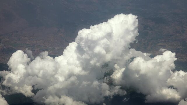 Aerial airplane view towering cumulus cloud above rugged terrain and wide evening atmosphere.