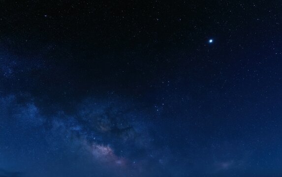 Deep blue night sky with dense star field and milky way band, bright planet shining among countless stars in cosmic darkness
