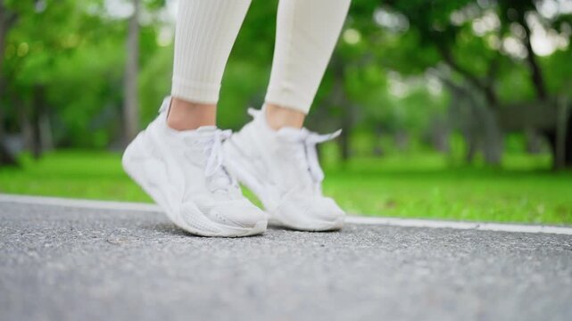 Close-up view foot of Asian woman tie shoelaces on road. Female runner sitting on floor in public park wearing sport shoes, tying shoelace before running