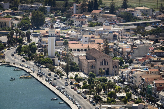 Aerial view of Agios Dionysios Church with its bell tower along the waterfront, featuring boats in the harbor, parked cars, and Mediterranean architecture in Zakinthos, Greece.
