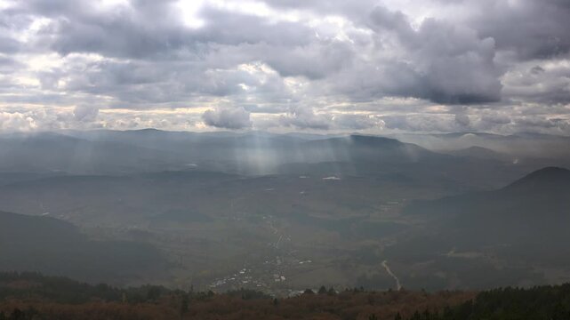 Isparta Turkey mountain peak overlooks a cone hill plain as clouds diffuse soft daylight rays.