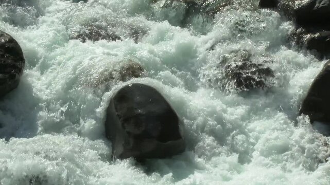 Foamy mountain river crashes against stones and rocks as turbulent whitewater surges downstream.