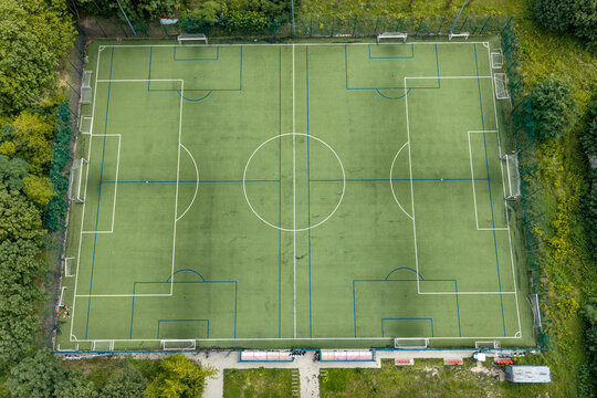 Aerial view of a football training field with green artificial turf, white markings, and surrounding trees in Poland.
