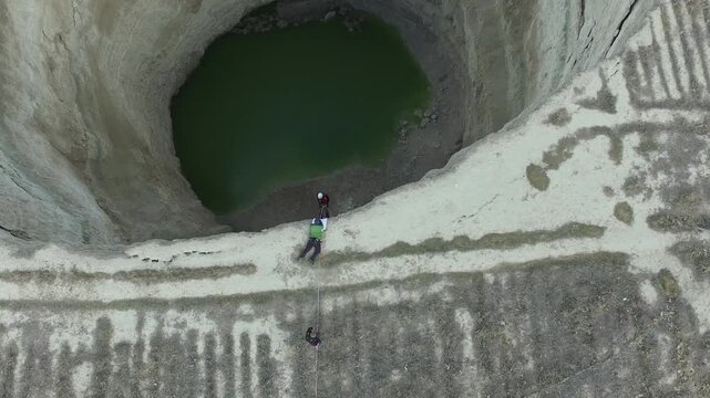 Deep sinkhole cave in aerial drone view as research team rappelling into vast geological well.