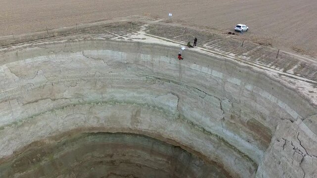 Deep sinkhole cave in aerial drone view as research team rappelling into vast geological well.