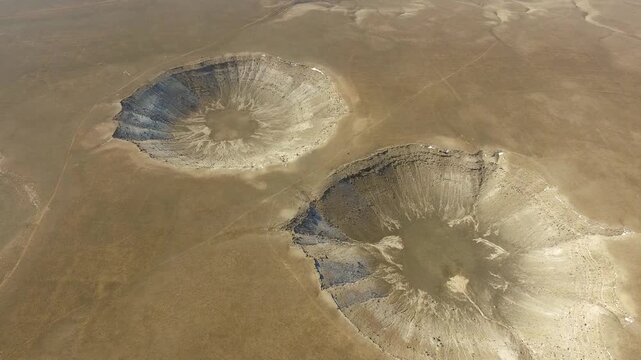 Aerial meteor craters across barren flat plain with dramatic impact geology under clear sky.