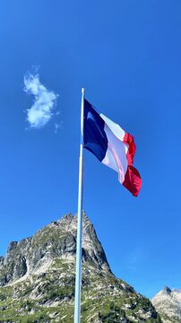 French flag waving against blue sky and mountain peak