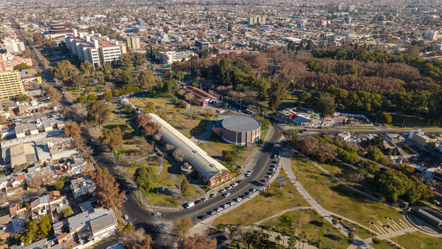 Aerial view of Parque de Mayo featuring its lush green spaces, mature trees, and distinctive circular and rectangular buildings surrounded by the urban landscape of San Juan, San Juan, Argentina.