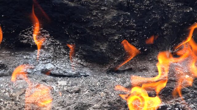 Natural methane gas fire burns between rocks on barren ground across a rugged rocky landscape.