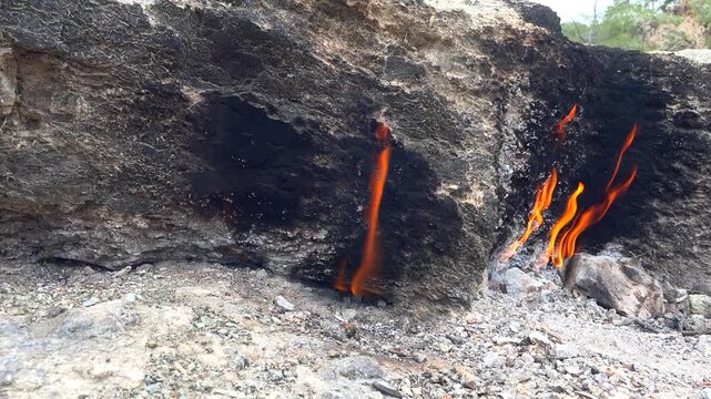 Natural methane gas fire burns between rocks on barren ground across a rugged rocky landscape.