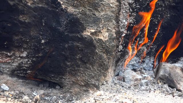 Natural methane gas fire burns between rocks on barren ground across a rugged rocky landscape.