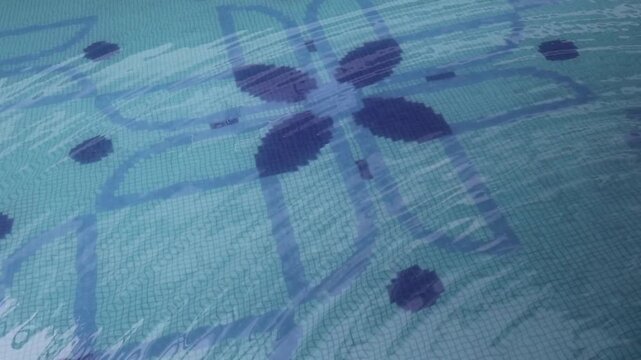 Swimming pool floor with blue mosaic tiles and abstract floral patterns visible beneath clear water. Aquatic texture, underwater geometric pattern, pool background, leisure facility detail