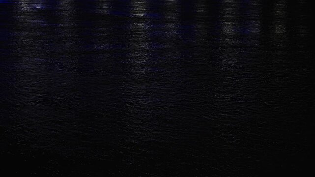 Dark water surface at night reflecting city and buoy lights.