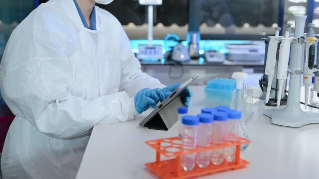 Focused researcher in protective lab gear examines scientific specimens using a stereo microscope in a modern biotechnology laboratory.