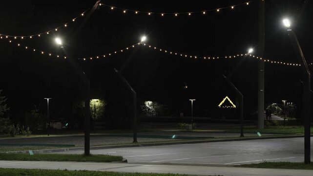 Empty night parking lot illuminated by string lights and lanterns.