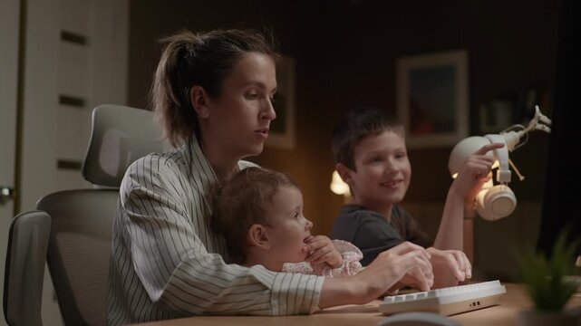 Working mother surrounded by children. Woman is working at computer typing with two children nearby distracting her. Work from home freelancer at work concept