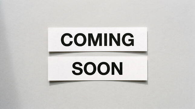 Two white paper signs with the words coming soon printed in black block letters on a neutral gray background