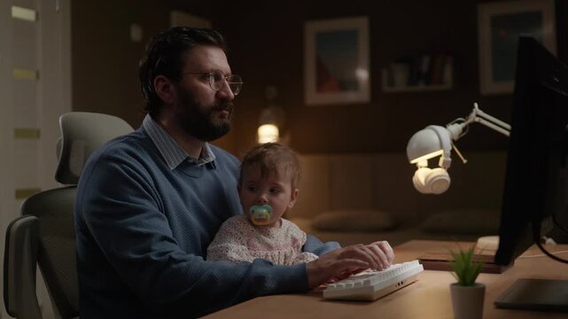 Family freelancer at work. Man with glasses working on computer in home office with young child sitting on his lap